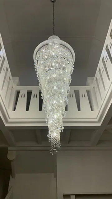 Crystal cascade chandelier hanging the full height of a white stairwell void above a painted balustrade