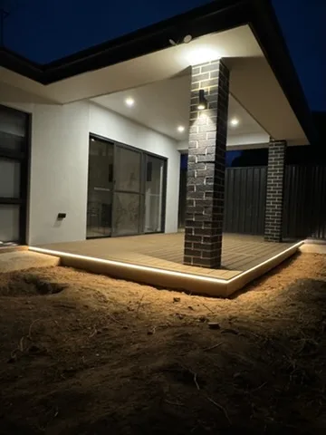 Soffit downlights and a continuous deck edge strip light glowing across a new alfresco at dusk