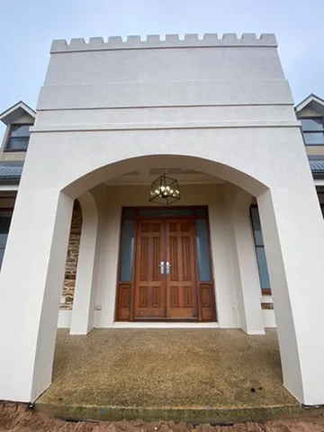 Small chandelier lighting the arched render portico above a solid timber front entrance door