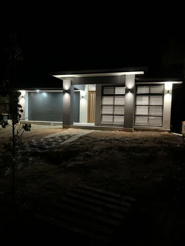 Six wall lights washing the piers and garage doors of a charcoal render facade after dark