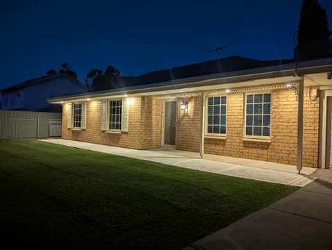 Wall lights along the front of a brick home at dusk with the lawn in shadow