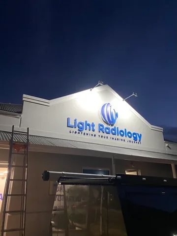 Sign floodlights aimed at a newly installed illuminated shopfront sign with the ladder still up