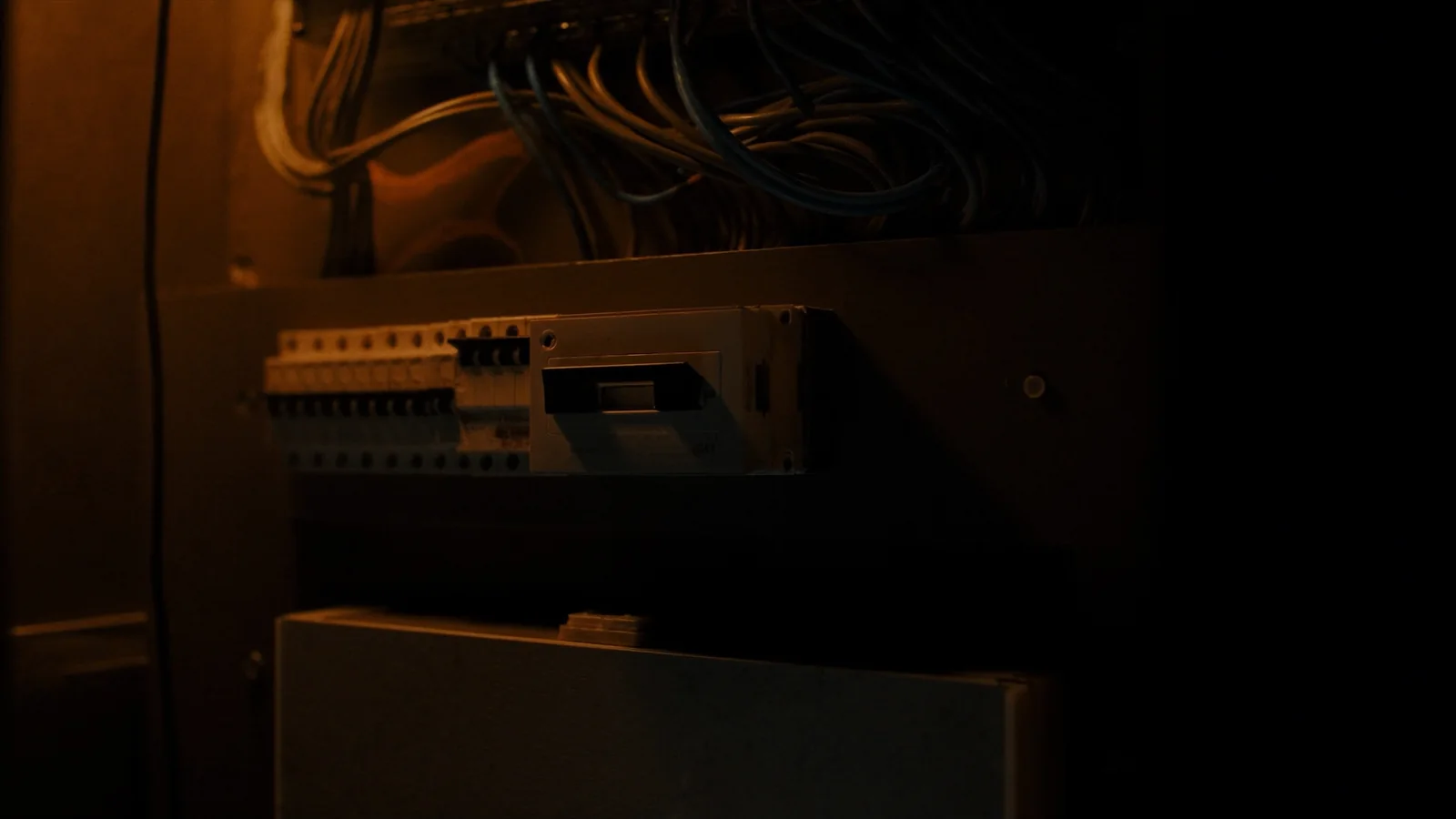 An open switchboard enclosure lit by torchlight, breakers and labelled circuits visible