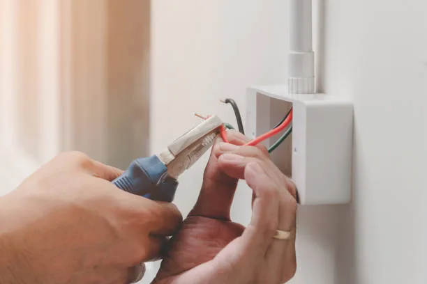 Hands terminating conductors into a power point with pliers before the cover goes on